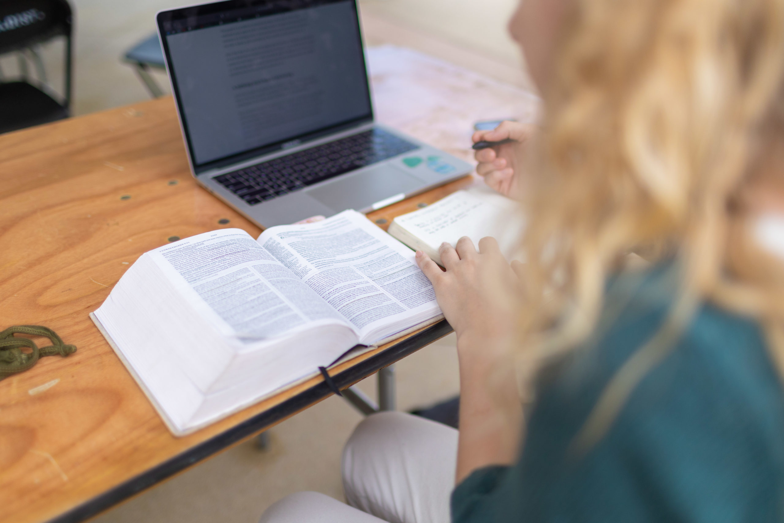 A young women reads an open bible with a notepad and a laptop